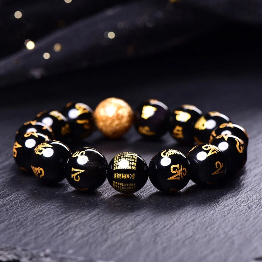 Buddhist mantra bracelet flat lay showing engraved scripture bead, gleaming gold foil centerpiece, and glossy obsidian beads arranged in circle