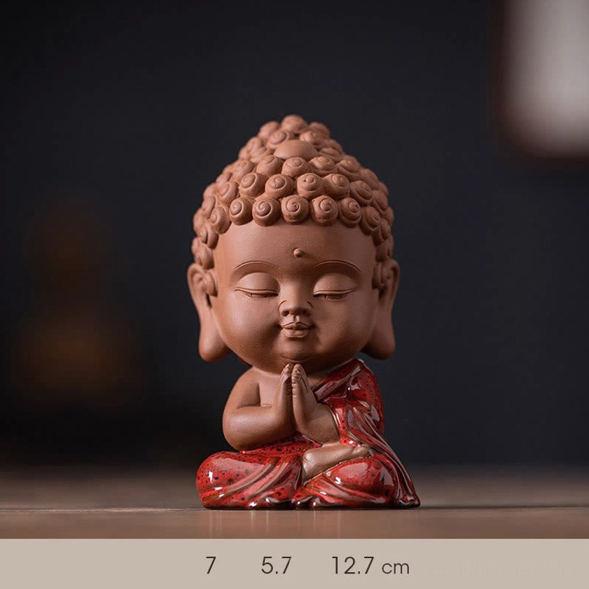 Front view of mini Sakyamuni Buddha ceramic figurine with prayer hands gesture and vibrant red glazed robes on wooden surface, showing size scale and measurement