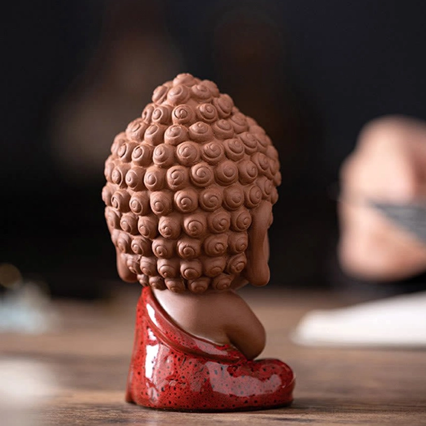 Rear view of mini Buddhist Sakyamuni figurine showing intricate curly hair buns detail and red glazed lower robes on wooden tabletop