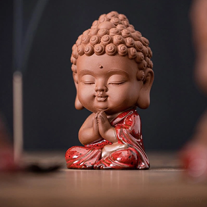 Three-quarter angle of Sakyamuni Buddha miniature figurine in peaceful meditation pose with closed eyes and prayer hands, displayed with incense stick on wooden table