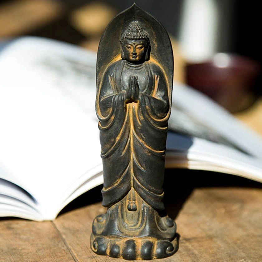 Sakyamuni Buddha Namaste statue front view with weathered bronze finish, intricate robe details and lotus base on wooden table