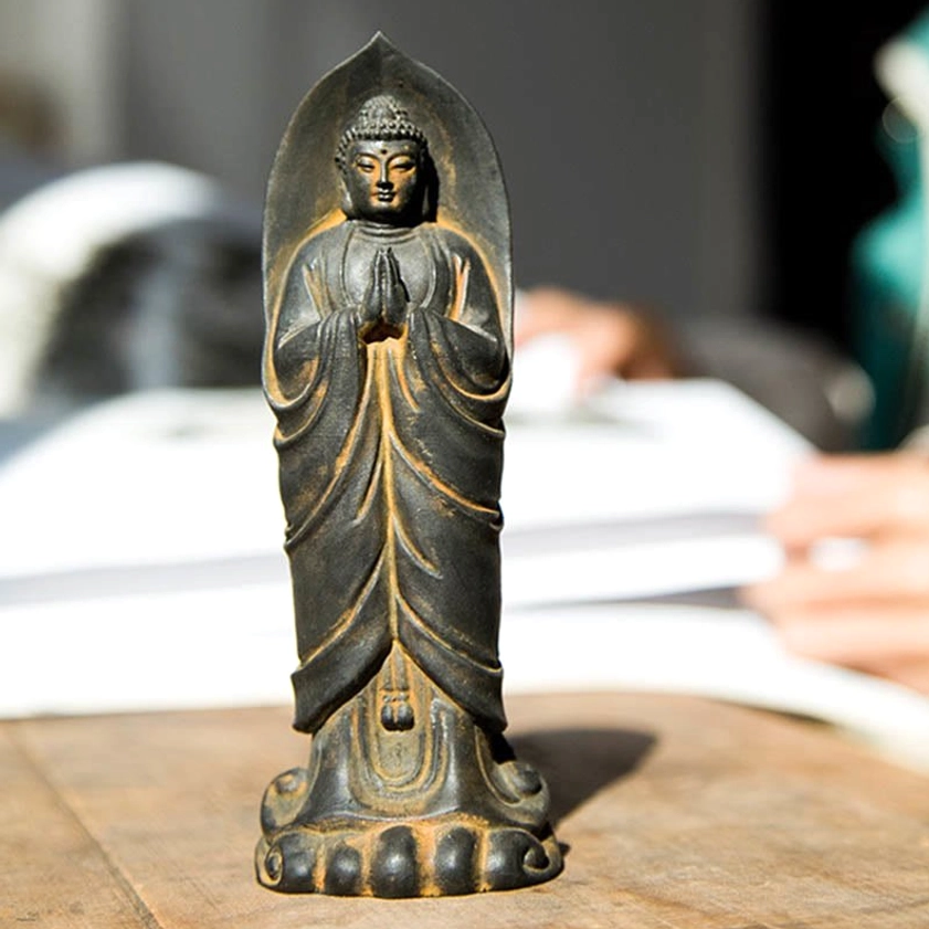 Sakyamuni Buddha Namaste statue front facing with soft lighting on wooden table, detailed prayer hands and spiritual ambiance