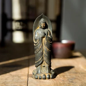 Handcrafted Sakyamuni Buddha Namaste statue with rust patina finish, front view displayed on wooden table with candle and spiritual setting