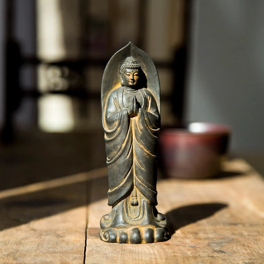 Handcrafted Sakyamuni Buddha Namaste statue with rust patina finish, front view displayed on wooden table with candle and spiritual setting