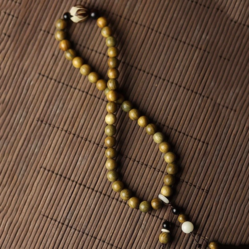 Twisted green sandalwood beaded necklace style loop displayed on traditional bamboo mat with mixed accent beads