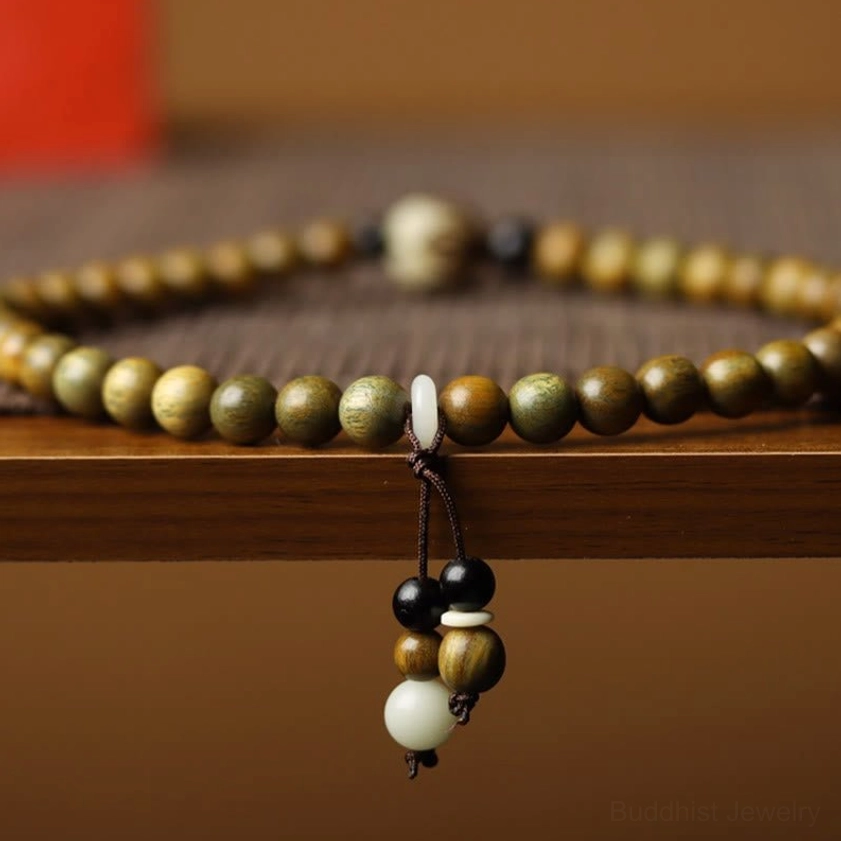 Flat lay of double wrap green sandalwood Buddhist bracelet with lotus tassel pendant on wooden surface showing bead detail