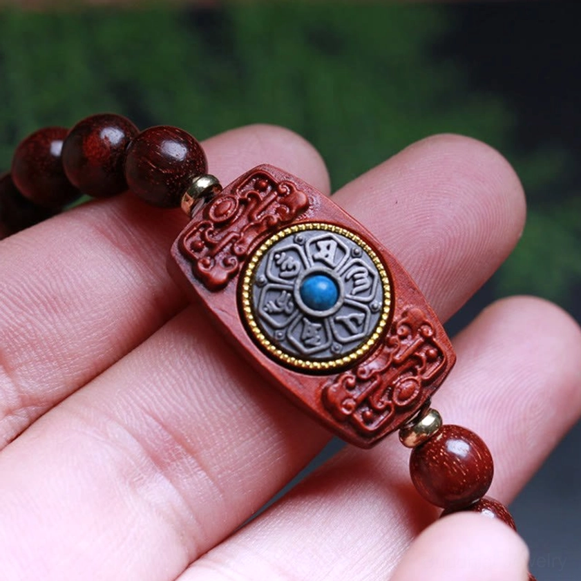 Buddhist sandalwood bracelet detail shot showcasing carved mantra charm with gemstone inlay