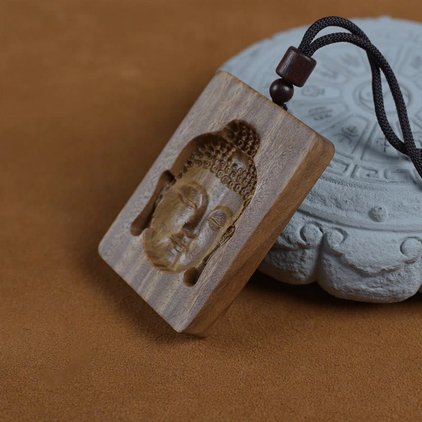 Three-quarter angle view of green sandalwood Buddhist pendant showing detailed Buddha face carving and authentic wood texture