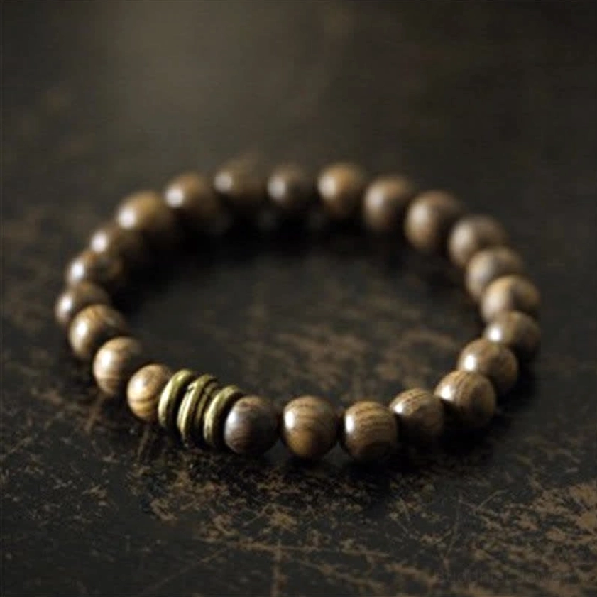 Sandalwood Buddhist protection bracelet with bronze metal spacers, three-quarter close-up view on dark vintage desktop