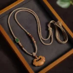 Sandalwood Buddhist lock charm necklace with braided cord and tassel, displayed on wooden jewelry tray