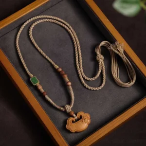 Sandalwood Buddhist lock charm necklace with braided cord and tassel, displayed on wooden jewelry tray