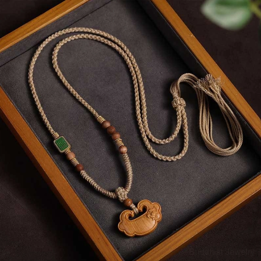 Sandalwood Buddhist lock charm necklace with braided cord and tassel, displayed on wooden jewelry tray