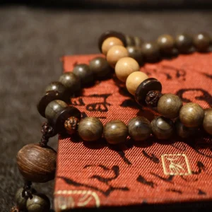 Handcrafted sandalwood Buddhist mala bracelet with 108 prayer beads, two-tone wooden beads with decorative tassel pendant, displayed on vintage red fabric