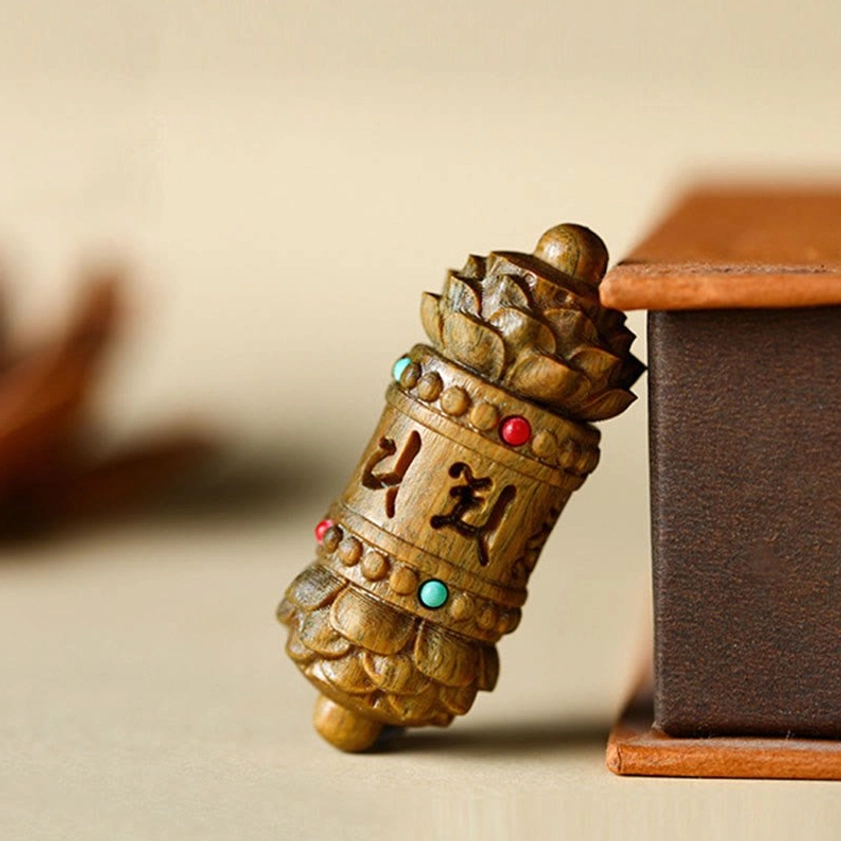 Side view of carved sandalwood Buddhist pendant showing intricate scripture details and green aventurine gemstone inlays on wooden display box