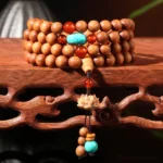 Sandalwood Buddhist prayer mala bracelet with 108 beads and lotus charm pendant displayed on carved wooden stand, high-angle close-up view