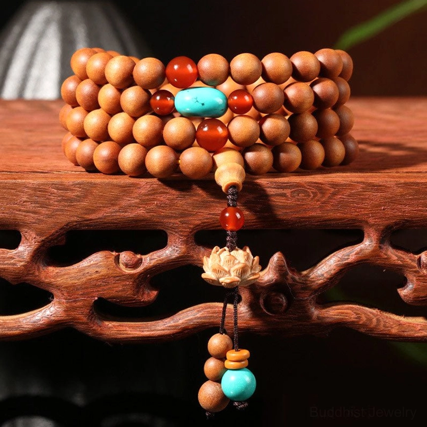 Sandalwood Buddhist prayer mala bracelet with 108 beads and lotus charm pendant displayed on carved wooden stand, high-angle close-up view
