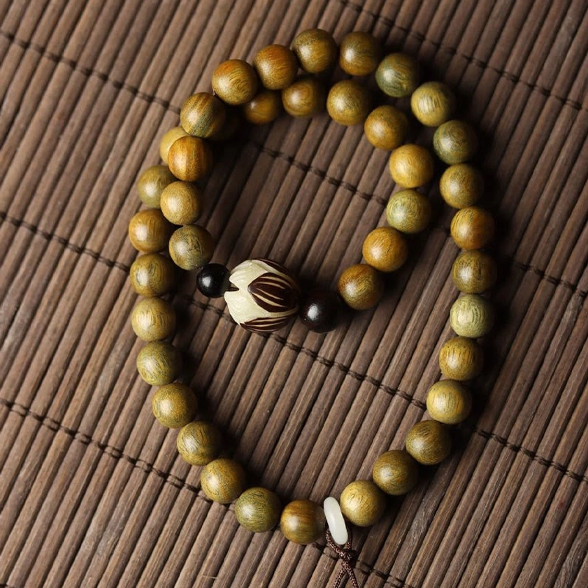 Green sandalwood double wrap bracelet on traditional bamboo mat displaying consistent wooden beads with carved lotus accent bead