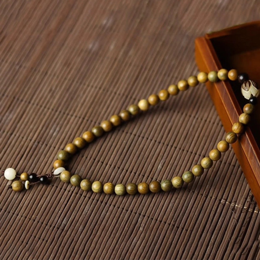 Long green sandalwood beaded strand with lotus accent pendant displayed on bamboo mat with wooden tray neat arrangement