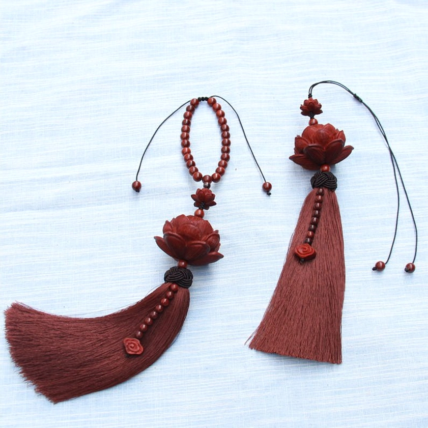 Two styles of handmade red sandalwood lotus tassels with different rope designs displayed on blue fabric