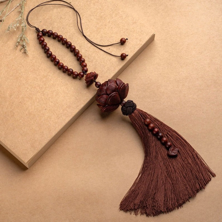 Side view of handcrafted red sandalwood lotus tassel with beaded ornament on neutral background