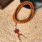 Red sandalwood Buddhist prayer mala with 10mm beads and red Chinese knot tassel, displayed on woven placemat