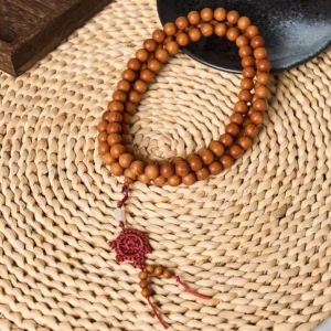 Red sandalwood Buddhist prayer mala with 10mm beads and red Chinese knot tassel, displayed on woven placemat