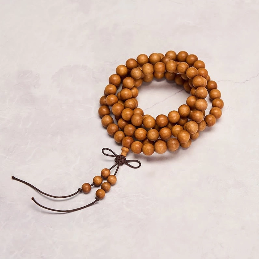 Light brown sandalwood prayer mala with dark brown bow-style tassel on grey background