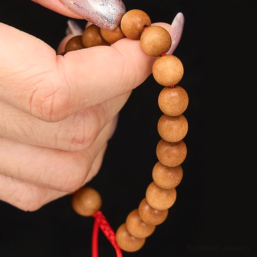 Detail view of sandalwood prayer beads mala showing smooth round wooden beads and red end knot on black background