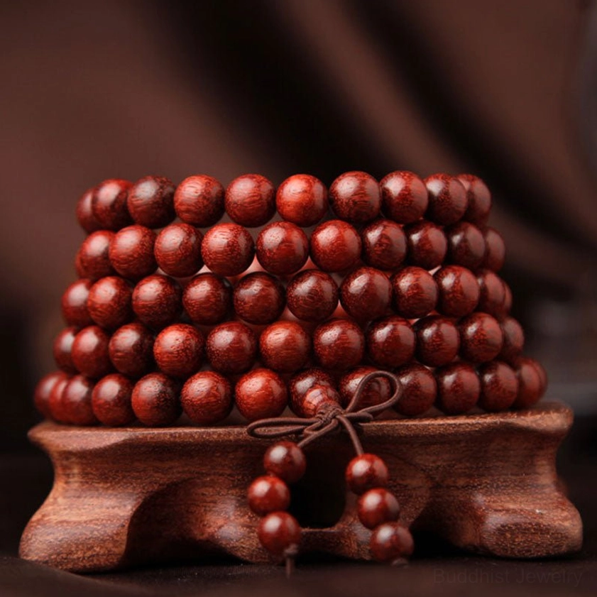 Red sandalwood meditation mala bracelet stacked display showing neatly arranged round beads and knotted tassel