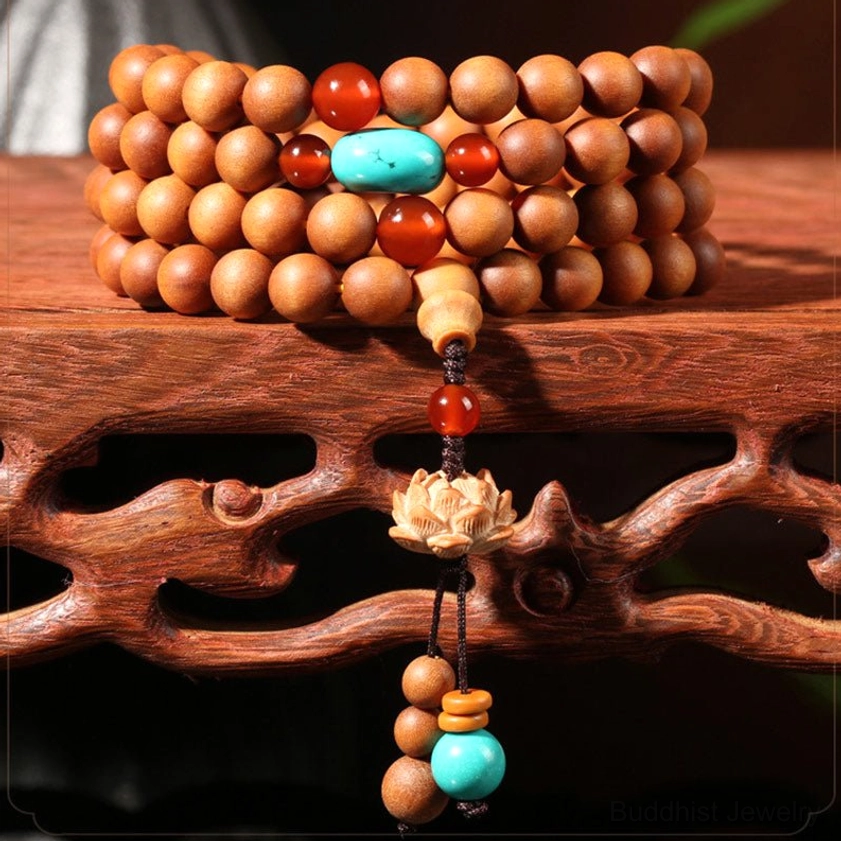 Front close-up of stacked sandalwood Buddhist prayer mala with red agate and turquoise bead accents, lotus charm tassel on wooden stand