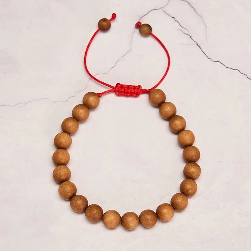 Premium sandalwood bead mala with smooth brown wooden beads and red woven knot fastener on marble surface