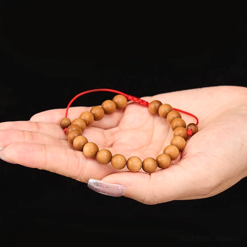 First-person palm display of sandalwood mala bracelet showing light brown wooden beads on hand with red adjustable cord