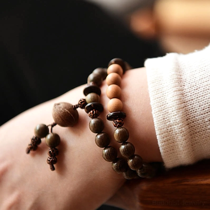 Two stacked handmade sandalwood mala bracelets worn on wrist, showing natural wood tones and decorative tassels, demonstrating wearable meditation practice