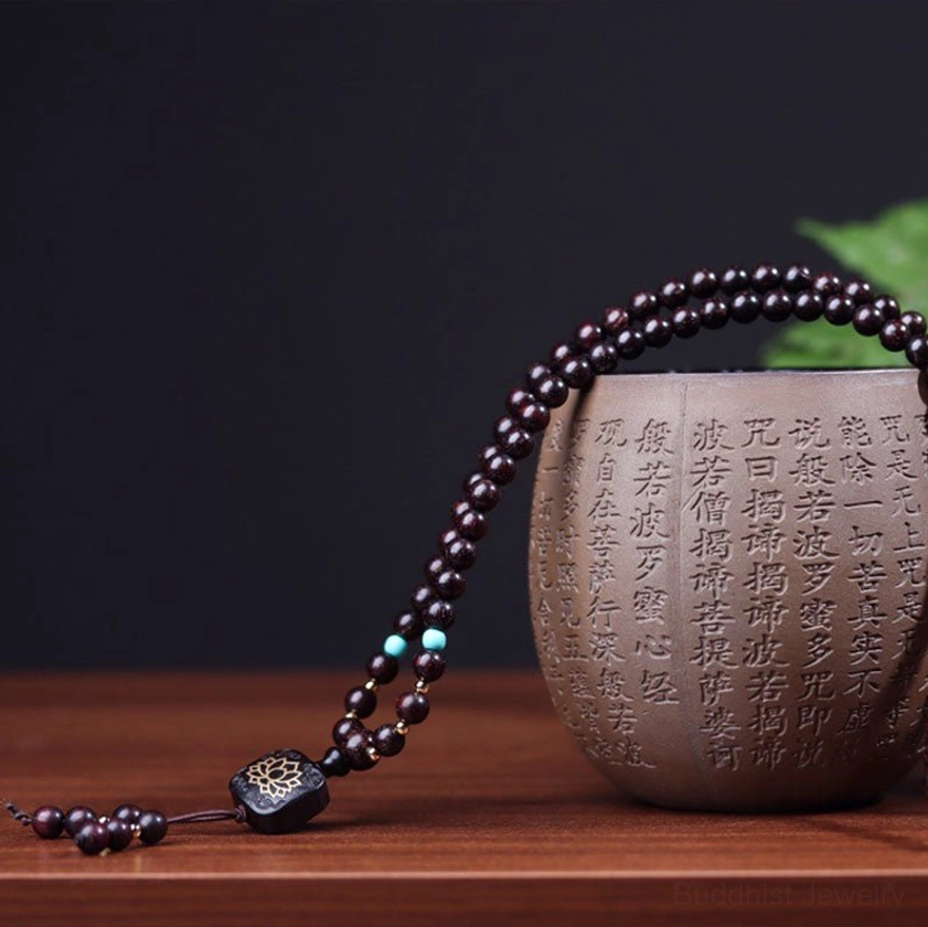 Red sandalwood mala bracelet displayed beside Buddhist tea cup showcasing zen-themed spiritual aesthetic