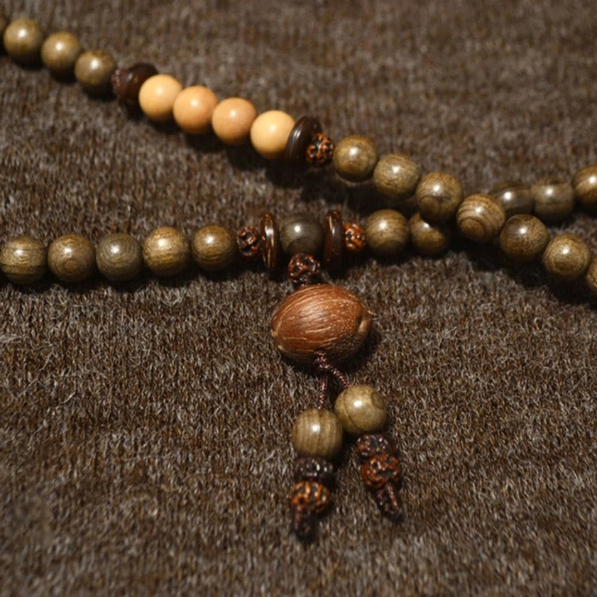 Sandalwood mala set featuring two-tone wooden beads with large wooden tassel pendant, close-up flat lay on brown textured fabric background