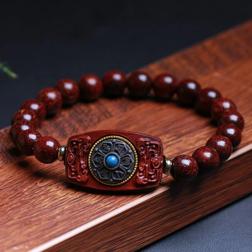 Red sandalwood Buddhist peace bracelet with glossy polished beads and engraved focal charm with blue accent, overhead flat lay