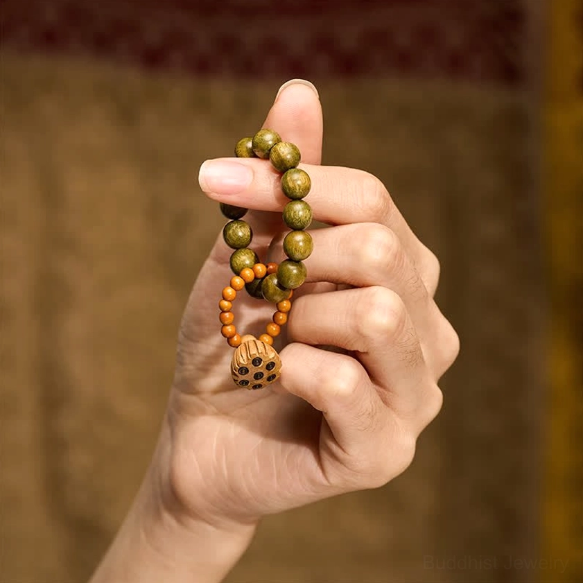 Sandalwood lotus meditation palm beads in hand-held first-person close-up view, showing green round beads, orange spacer beads, and detailed carved lotus charm