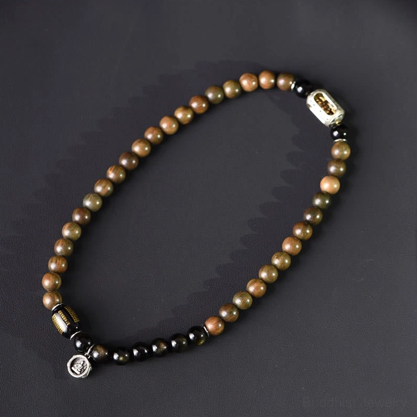 Single strand variation of sandalwood and obsidian beaded bracelet with metal accents on dark background
