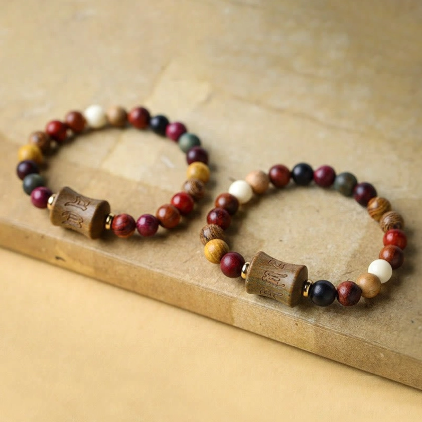 Two matching multicolor sandalwood Buddhist bracelets with carved focal beads, flat lay on wooden surface