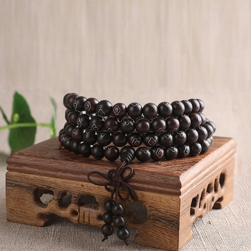 Multi-loop red sandalwood mala bracelet with silver inlaid sacred characters and decorative tassel on wooden base