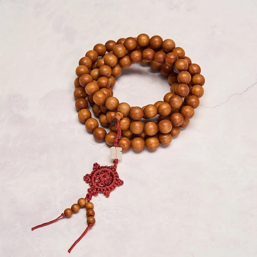 Long strand red sandalwood Buddhist mala with bright red decorative knot on marble surface