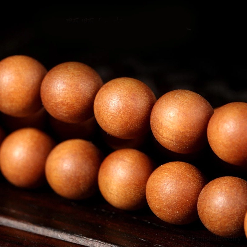 Extreme close-up macro view of polished uniform round sandalwood prayer beads on dark wooden surface, showing texture and grain detail