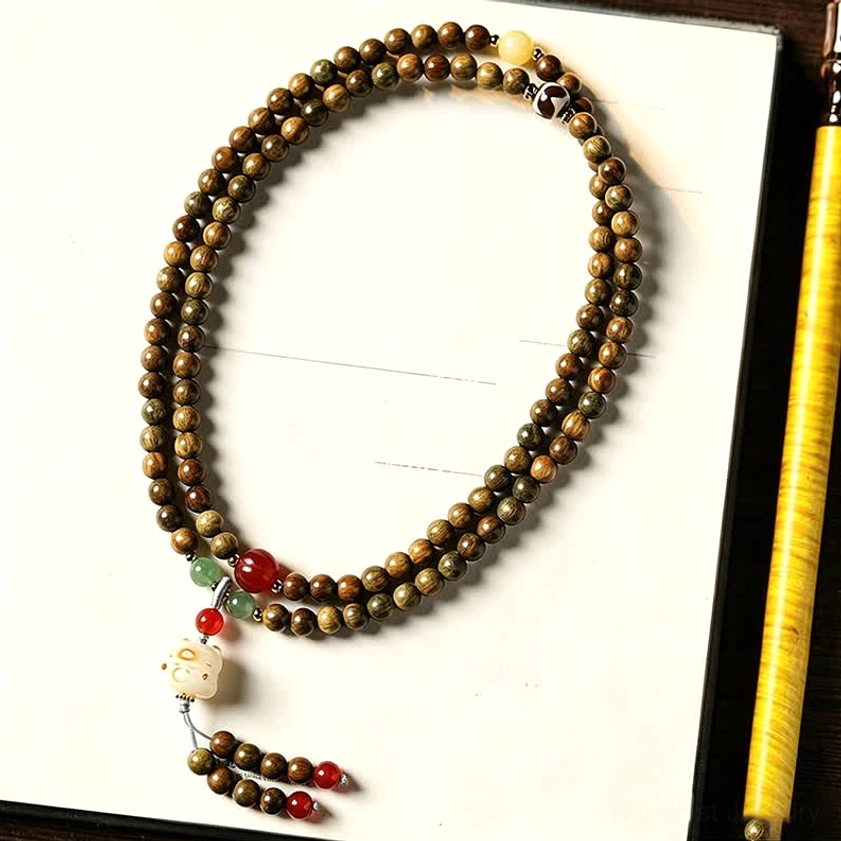 Brown sandalwood prayer beads mala with cat charm and red-green accents, flat lay on white paper background