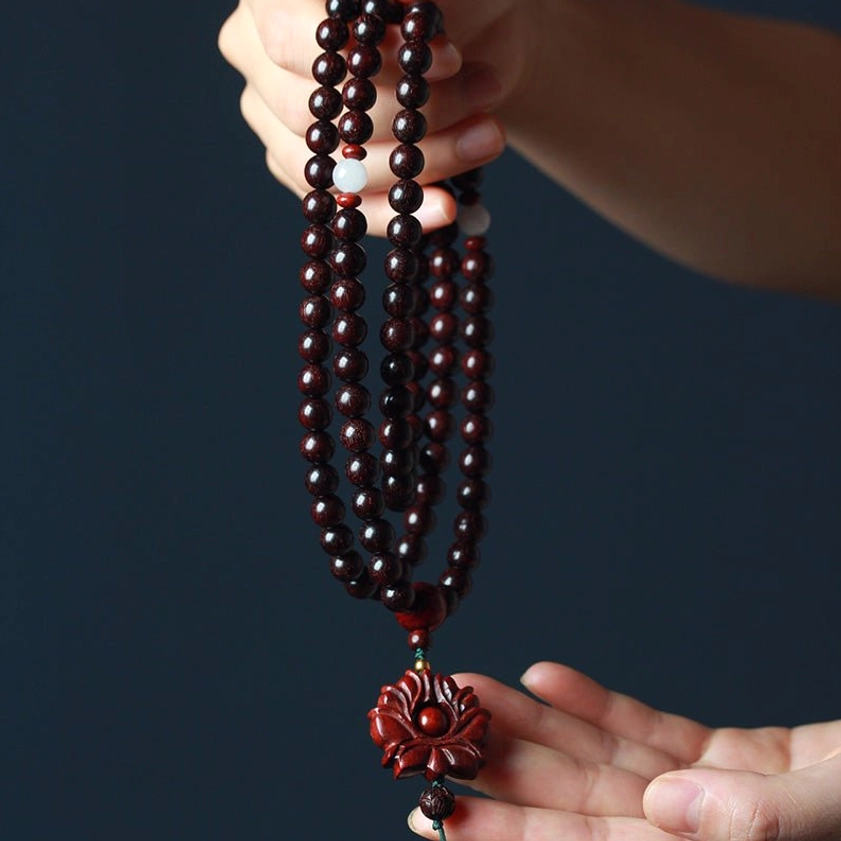 Close-up of hands holding 108-bead sandalwood mala showing polished wood texture white spacer beads and carved lotus pendant