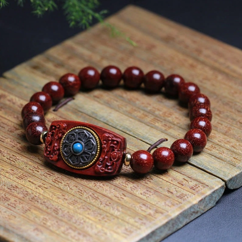 Polished red sandalwood beads with detailed carved focal charm featuring blue inlay, laid on bamboo wooden planks