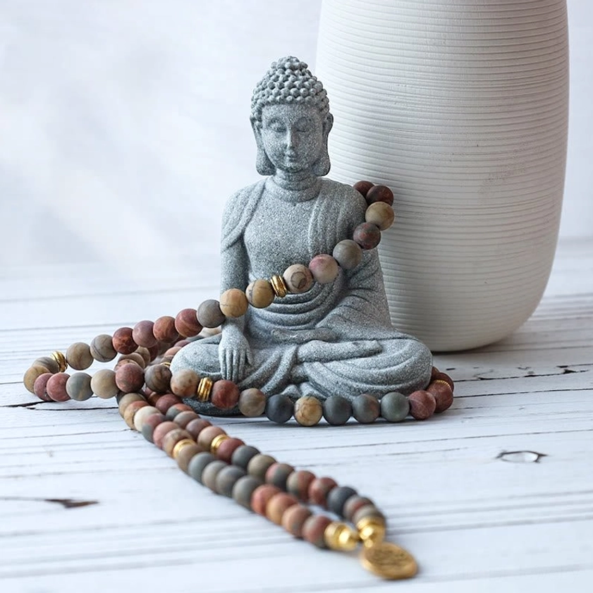 Meditation Buddha statue in sandstone with draped mala prayer beads and ceramic vase, oblique side view showing spiritual altar setup