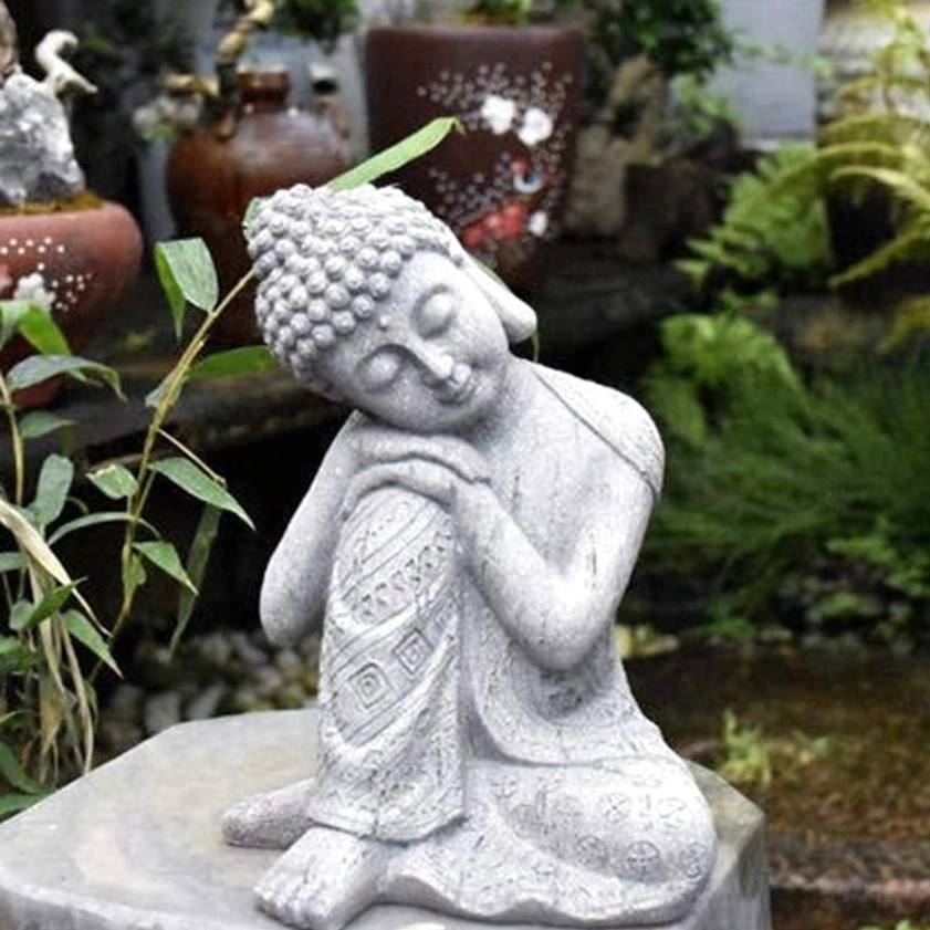 Seated Buddha statue with closed eyes and detailed carved robe in outdoor garden with potted plant decoration