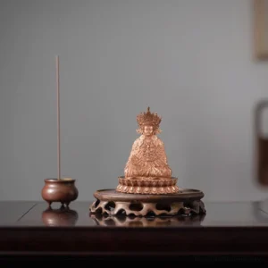 Handcrafted copper Shakyamuni Buddha statue with ornate crown and lotus pedestal displayed on dark wooden table next to traditional incense censer
