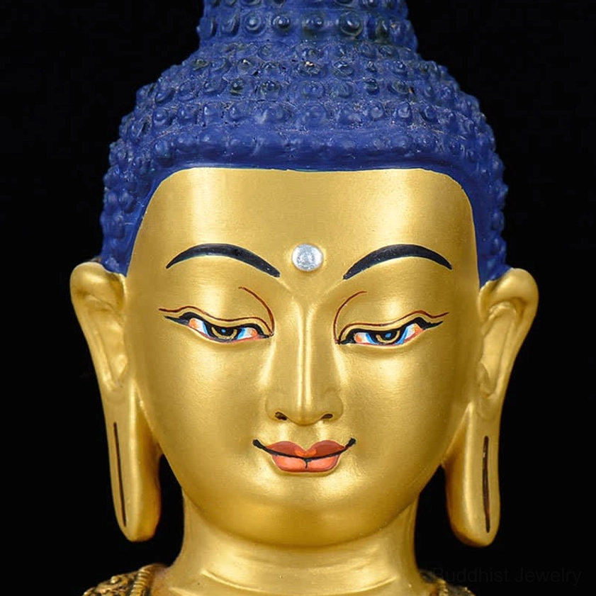 Shakyamuni Buddha statue head close-up showing blue curly hair, painted facial features, and white forehead gem detail