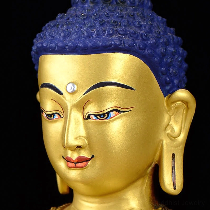 Shakyamuni Buddha statue head profile close-up displaying painted eyes, eyebrows, ear details with blue hair against black background